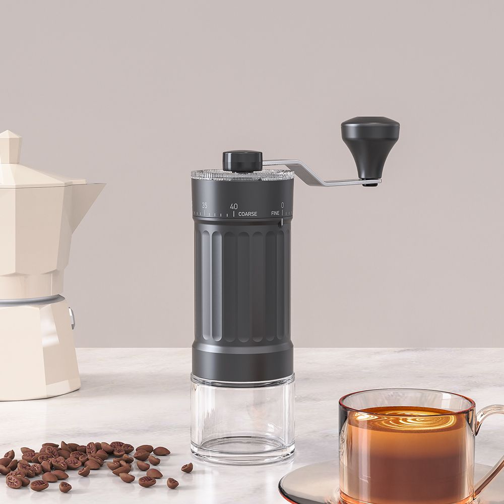 The Ermona hand grinder beside a moka pot and a glass of coffee.