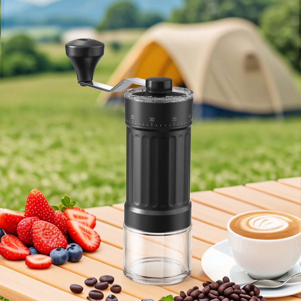 The Ermona hand coffee grinder on a wooden table outdoors with fresh berries and a latte, a tent in the background.