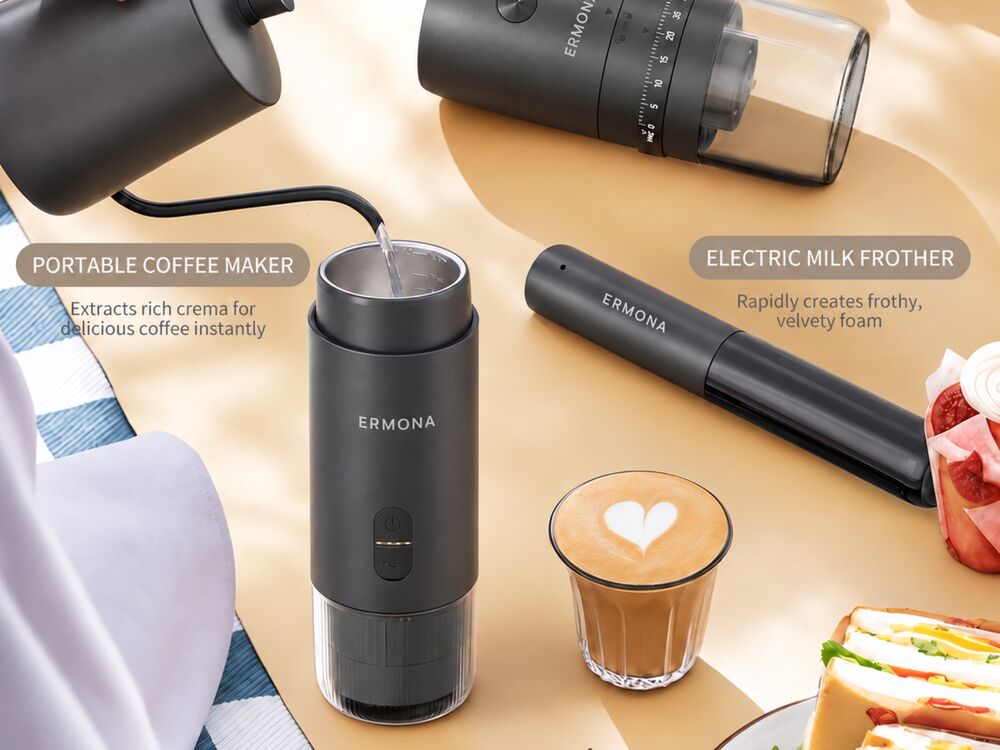 Hot water from a kettle poured into the Ermona portable espresso maker on a picnic blanket, with the milk frother, electric grinder and a latte nearby.